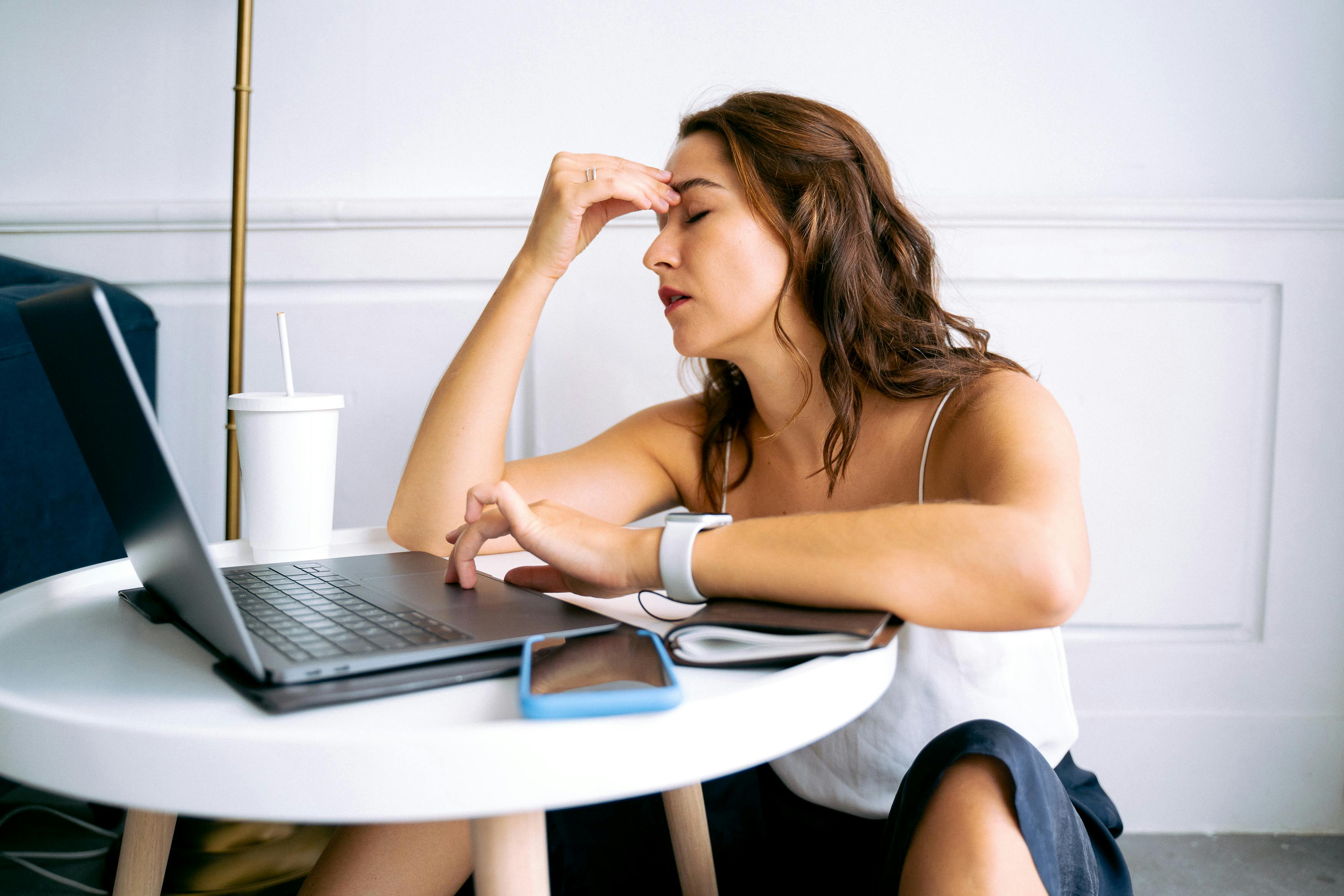 Woman sitting at her laptop holding her head, looking tired and fatigued
